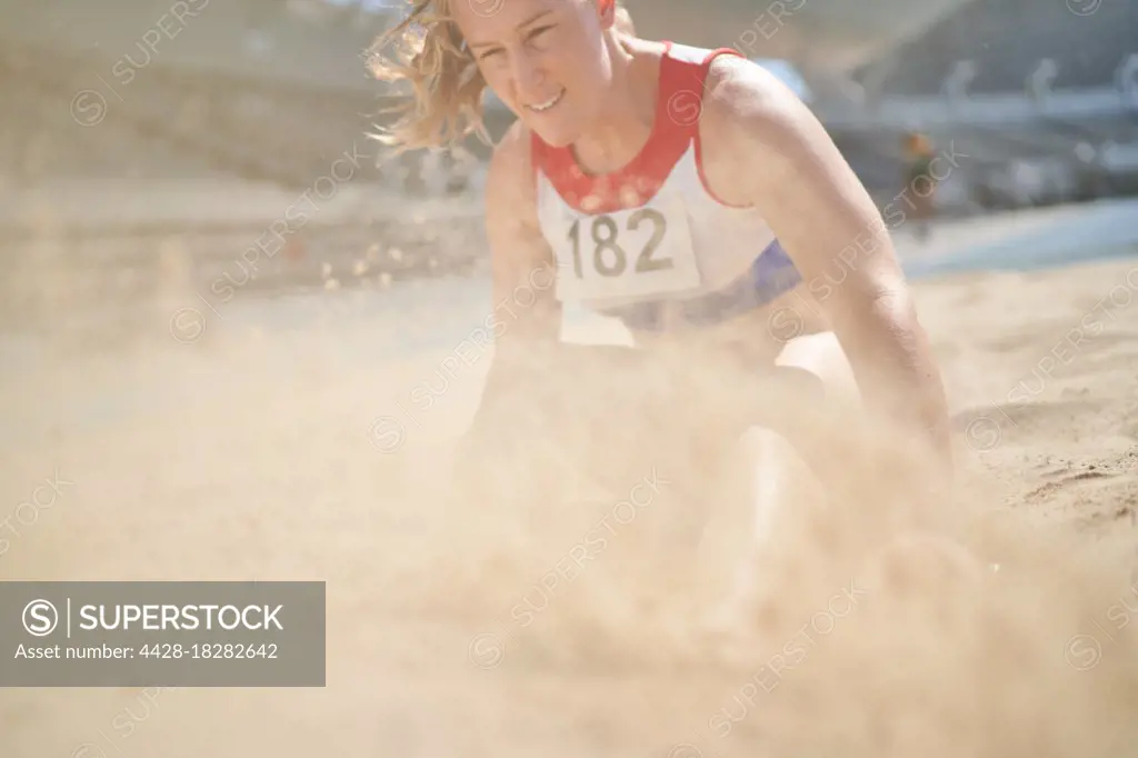 Female track and field athlete landing in long jump sand