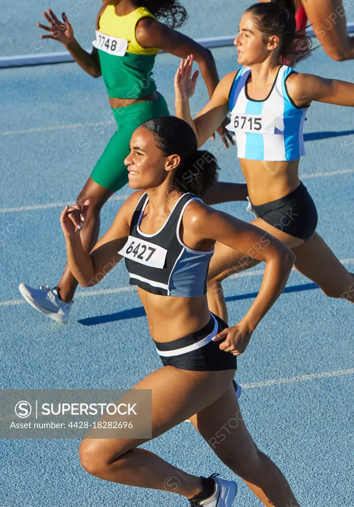 Female track and field athletes running on sunny track