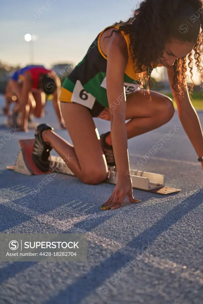 Female track and field athlete preparing at starting block on track