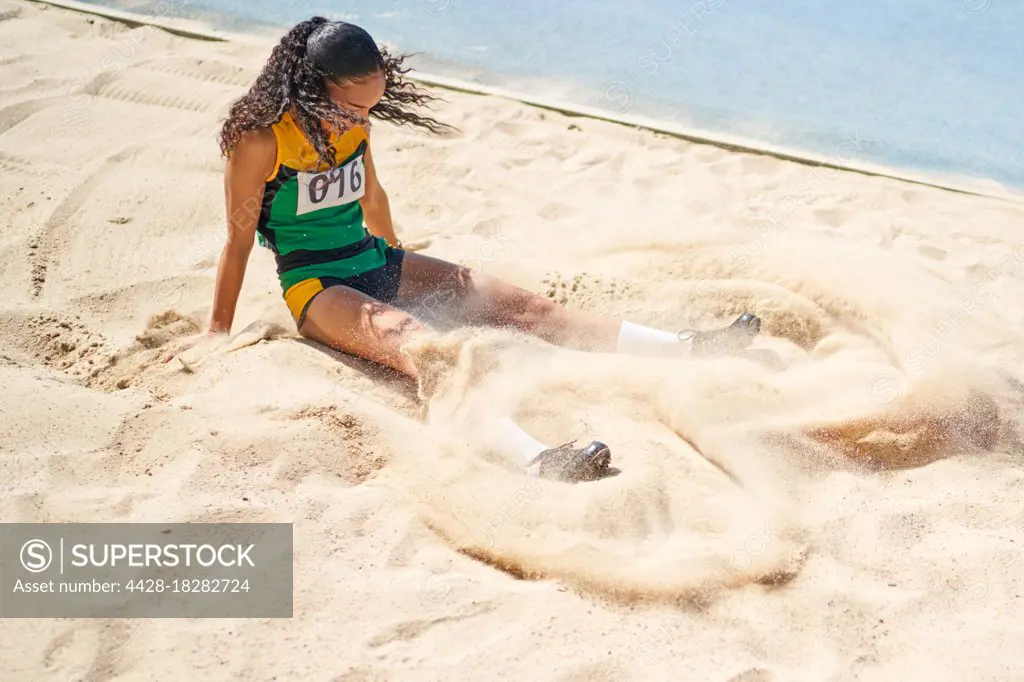 Female track and field athlete long jumping into sand