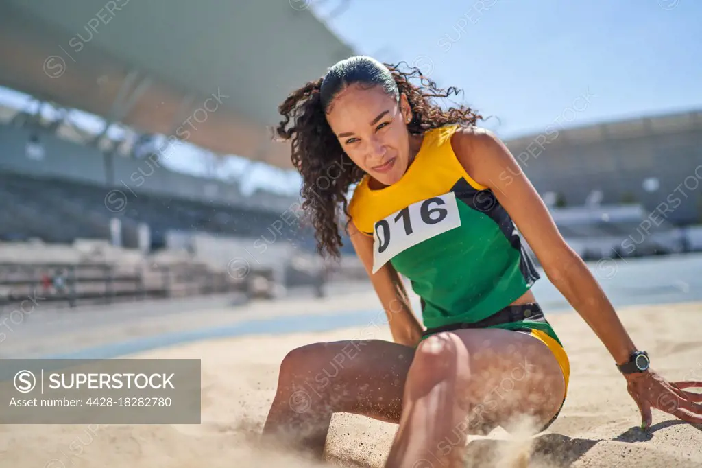 Female track and field athlete long jumping in sand