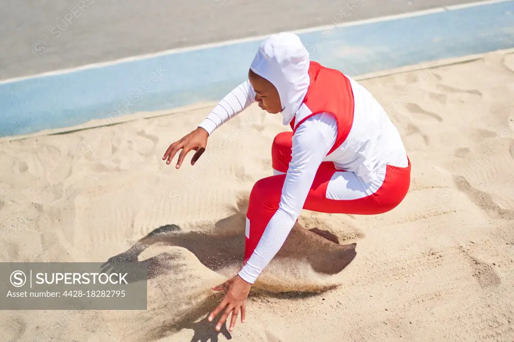 Female track and field athlete in hijab long jumping in sand