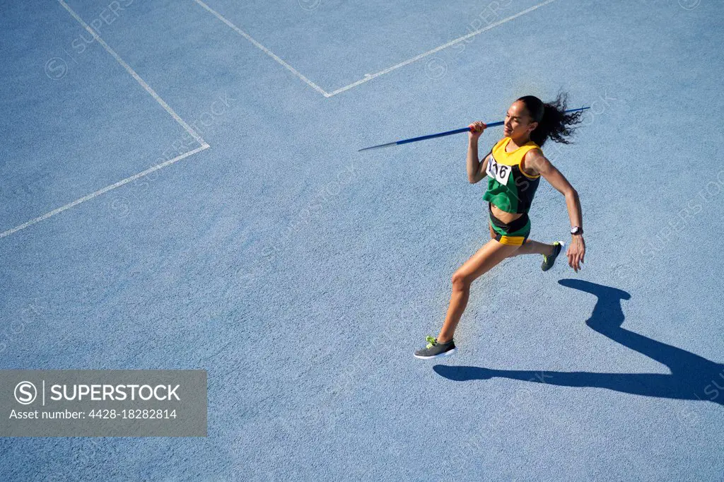 Female track and field athlete throwing javelin on sunny blue track