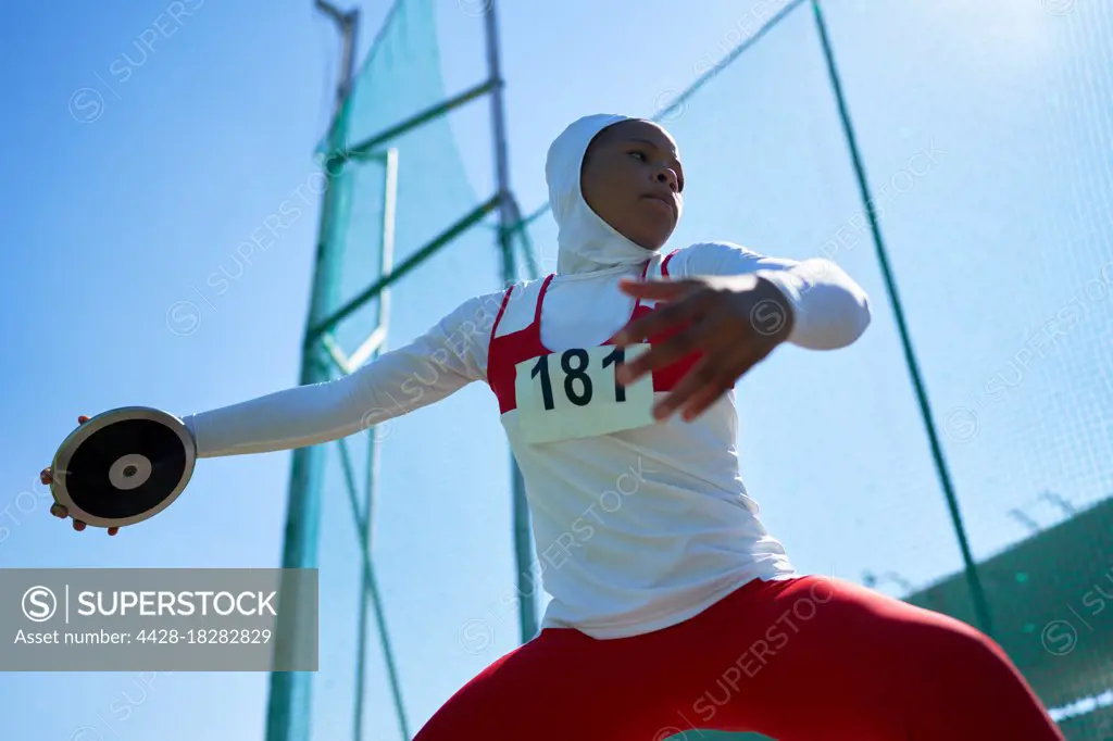 Determined female track and field athlete in hijab throwing discus