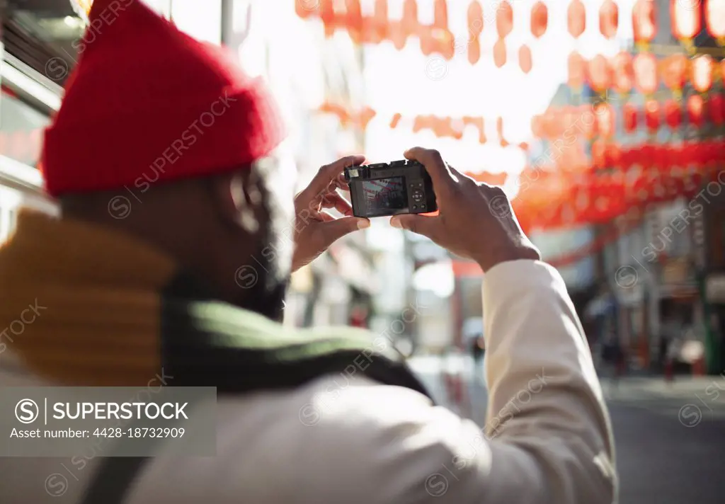 Male tourist with digital camera photographing paper lanterns in city