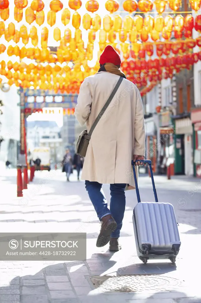 Male tourist pulling suitcase on sidewalk in Chinatown, London, UK