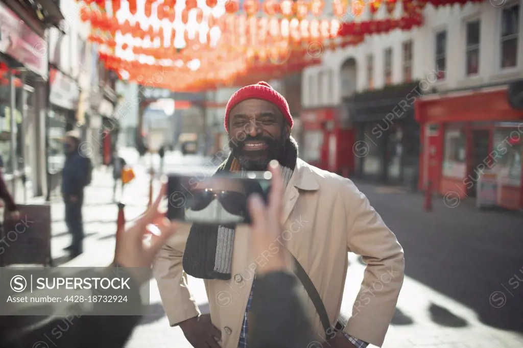 Woman in face mask photographing happy man on sunny city street