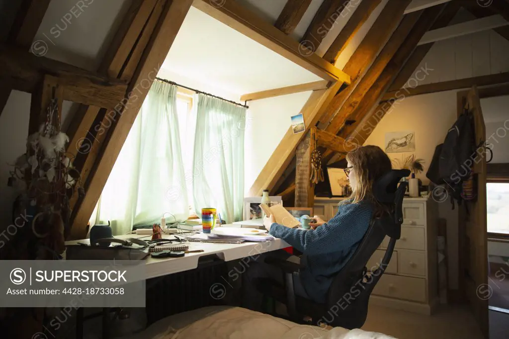 Woman reading book at desk in home office