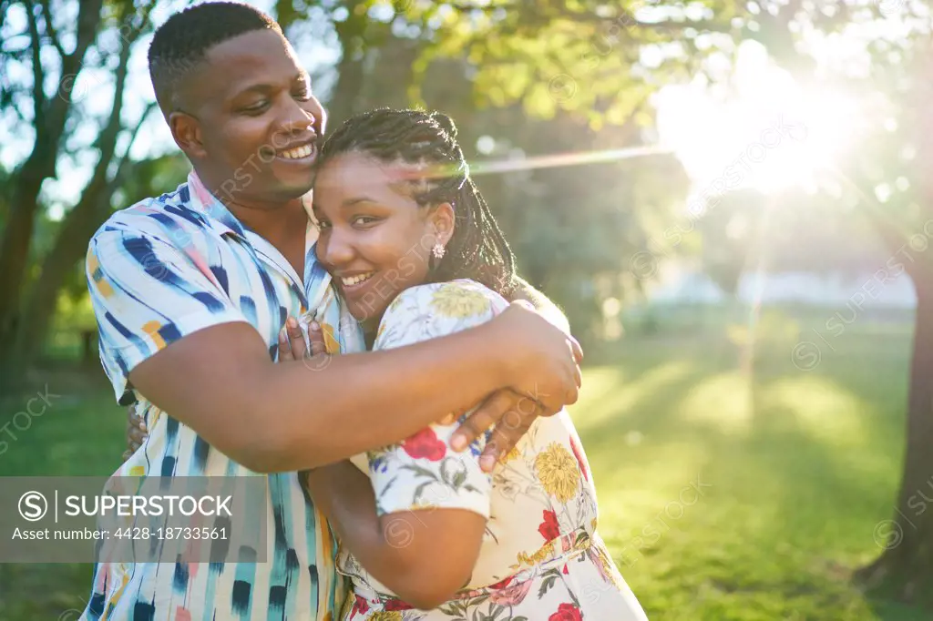 Portrait happy couple hugging in sunny summer park