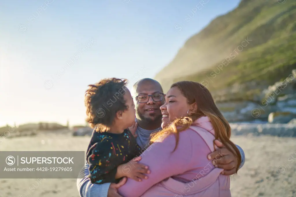 Happy parents and son hugging on sunny beach