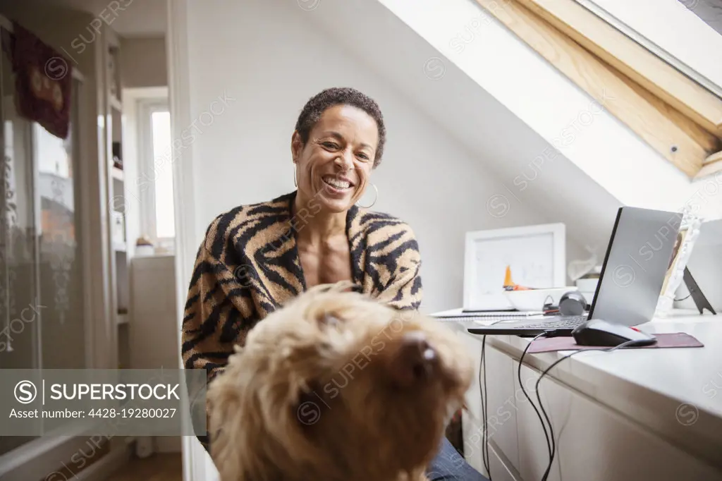 Portrait happy woman with dog at desk in home office