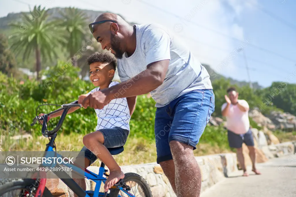 Father teaching happy son how to ride a bike on sunny boardwalk