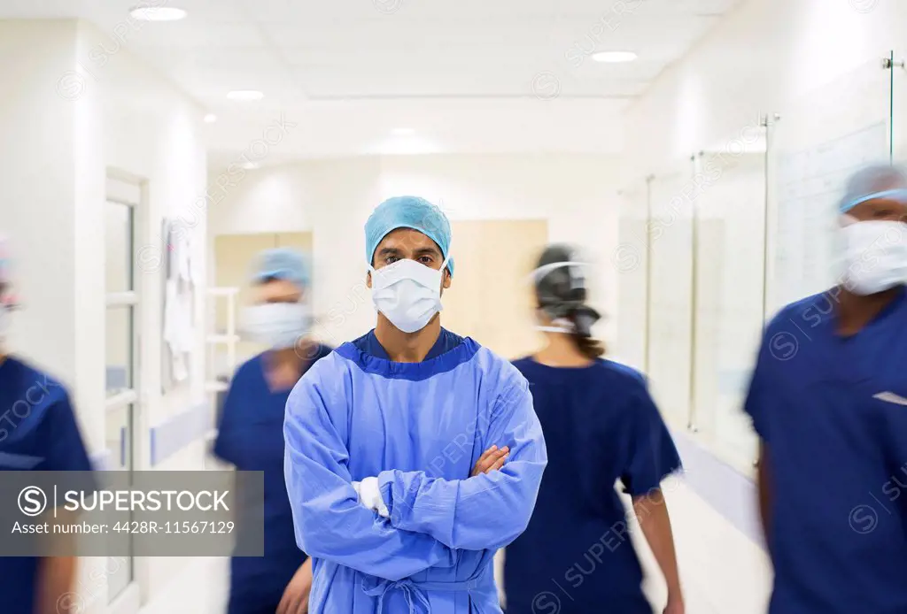 Surgeon with arms crossed, wearing scrubs standing in hospital corridor