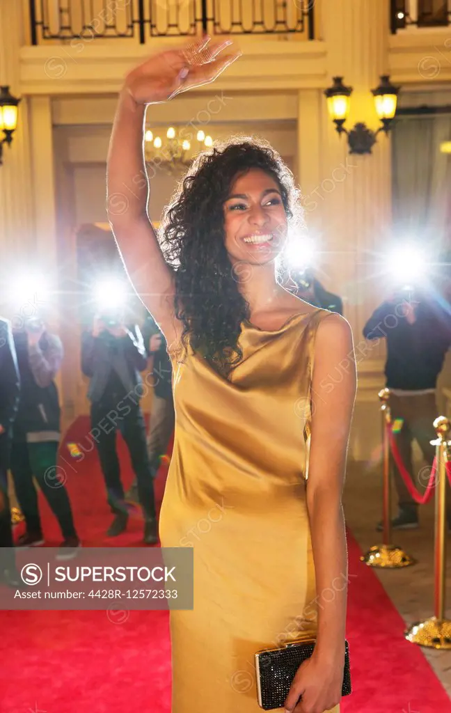 Smiling celebrity waving to paparazzi photographers at red carpet event