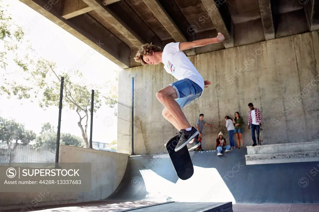 Teenage boy flipping skateboard at skate park