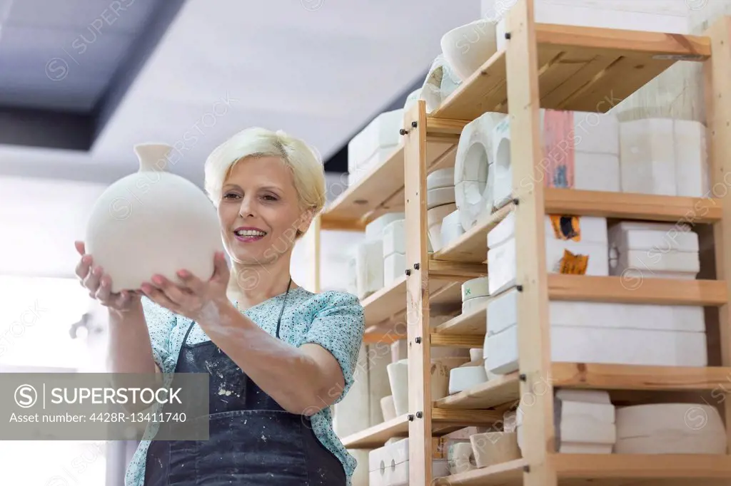 Smiling woman holding pottery vase in studio