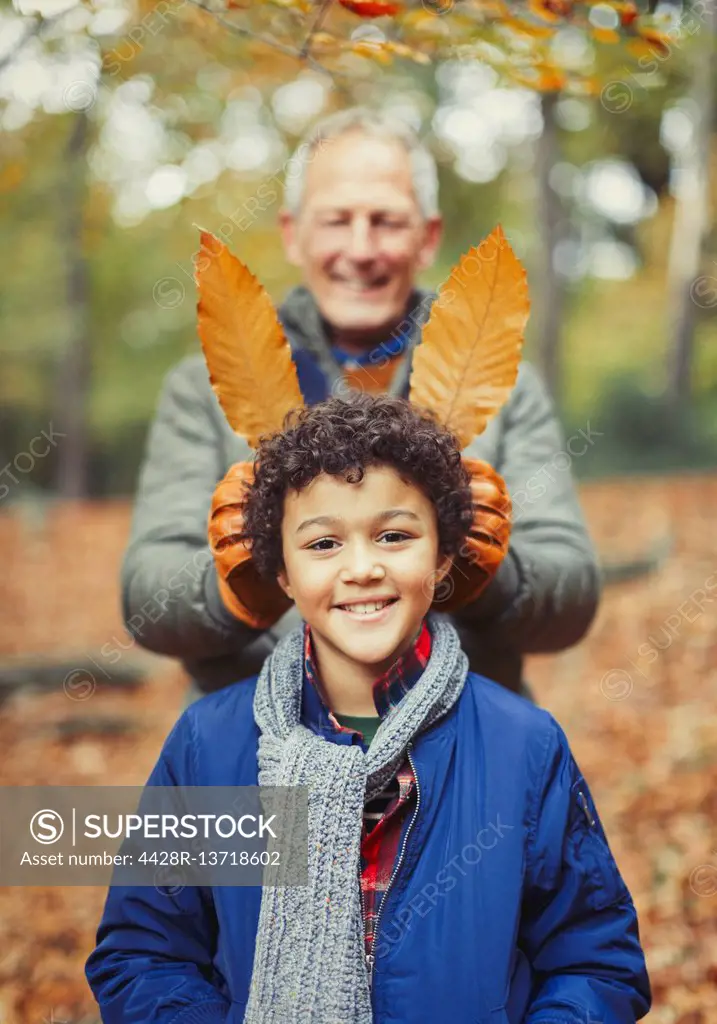 Grandfather holding autumn leaves behind grandson in woods