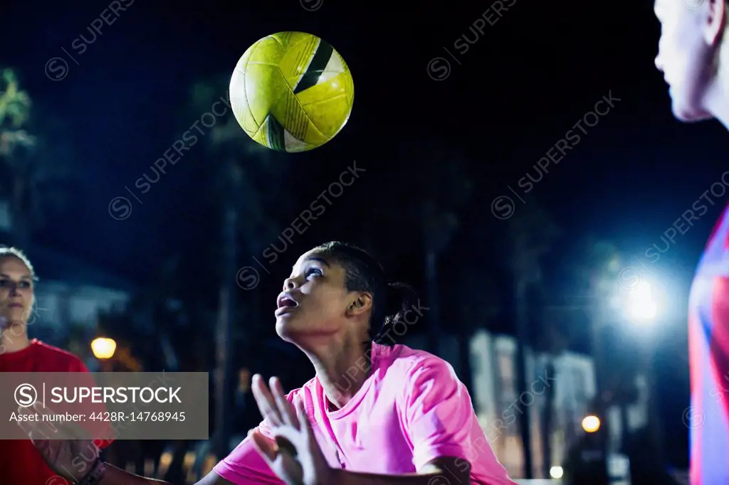 Young female soccer player heading the ball on field at night