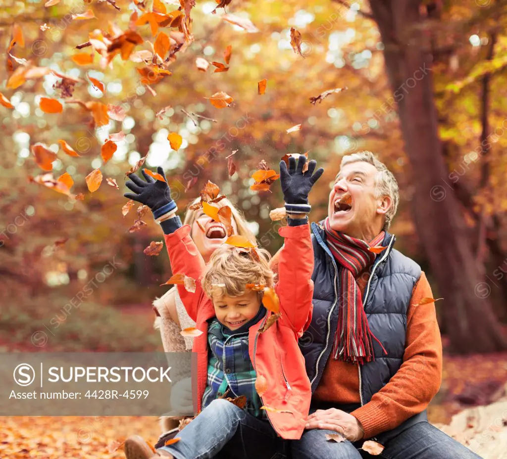 Older couple playing with grandson in autumn leaves,London, UK