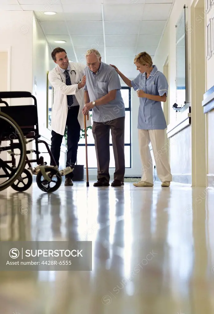 Doctor and nurse helping older patient walk in hospital