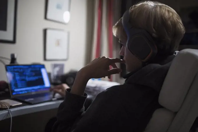 Teenage boy with headphones using computer in dark bedroom