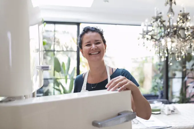 Portrait happy woman at open refrigerator in kitchen