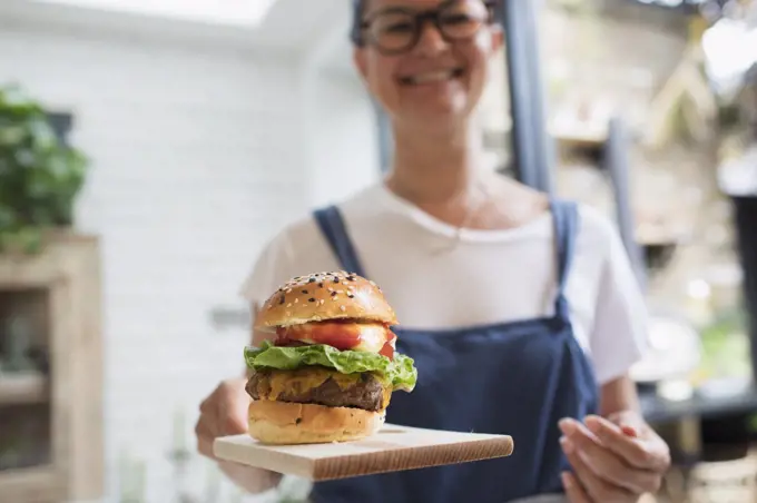 Portrait smiling woman with cheeseburger on cutting board