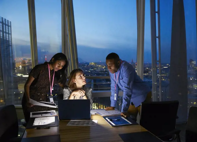 Business people working late at laptop in highrise conference room