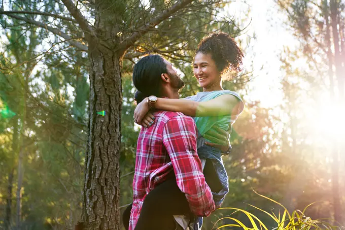 Affectionate young man holding happy girlfriend in sunny woods