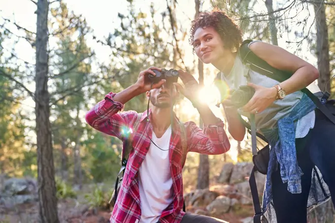 Curious young hiker couple using binoculars and camera in sunny woods