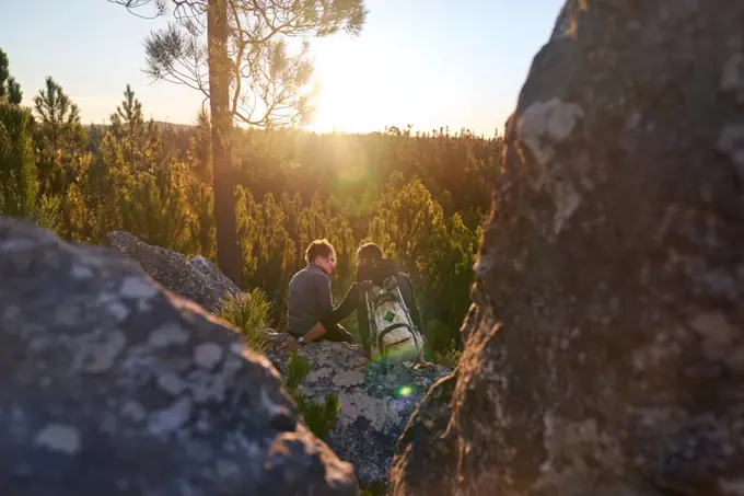 Affectionate young hiker couple relaxing on rock in sunny sunset woods