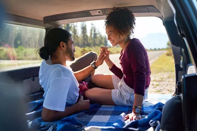 Happy affectionate young couple holding hands in back of sunny car