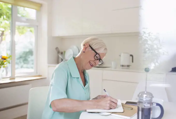Senior woman writing in journal at morning kitchen table