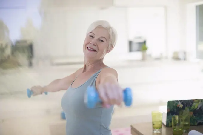 Portrait confident senior woman exercising with dumbbells in kitchen