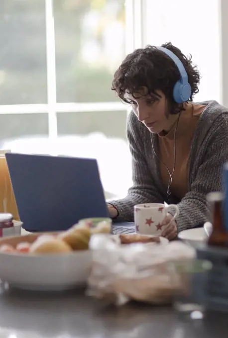Woman with headphones working from home at laptop in kitchen