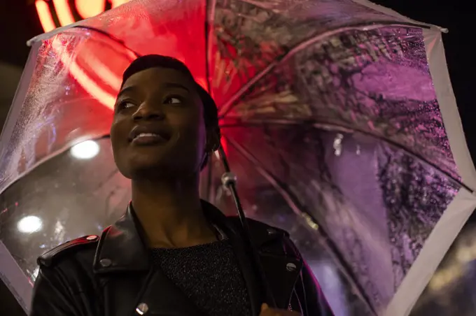 Smiling young woman under umbrella and neon sign at night