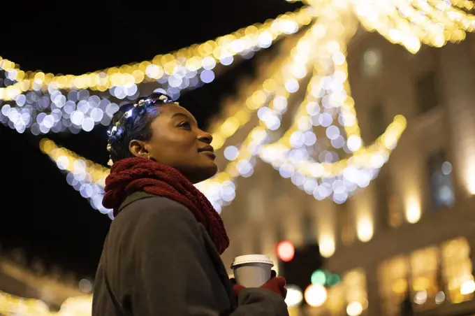Serene young woman with coffee in city with lights at night