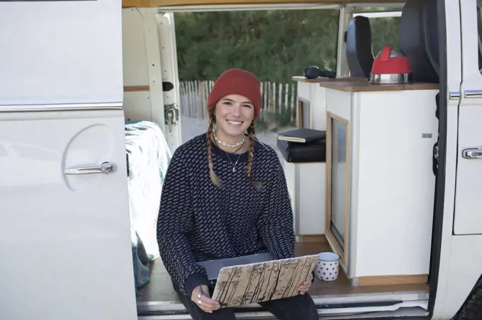 Portrait happy young woman with laptop in camper van doorway