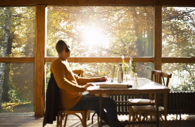 Businessman with headphones working at laptop in sunny autumn cafe