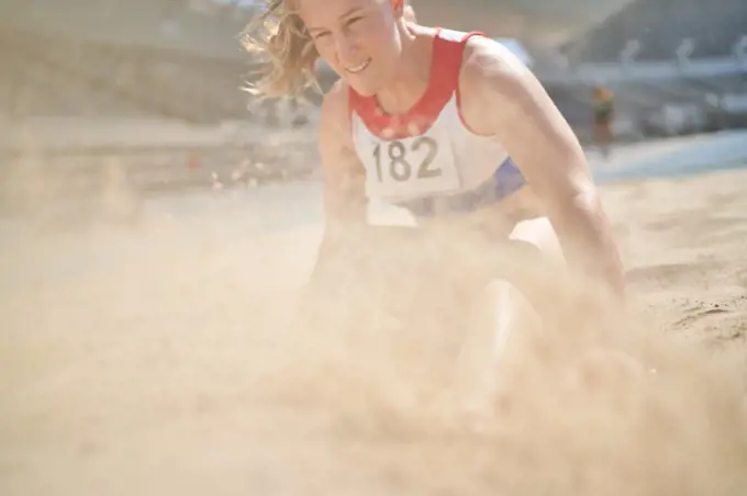 Female track and field athlete landing in long jump sand