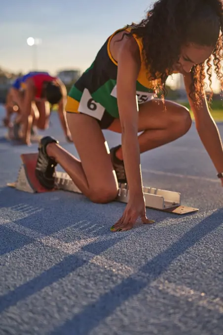 Female track and field athlete preparing at starting block on track