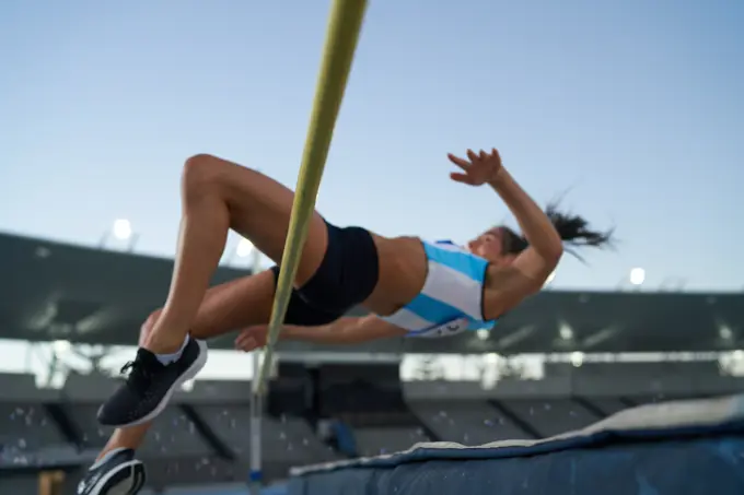 Female track and field athlete high jumping over pole