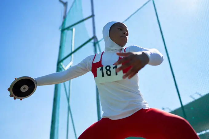 Determined female track and field athlete in hijab throwing discus