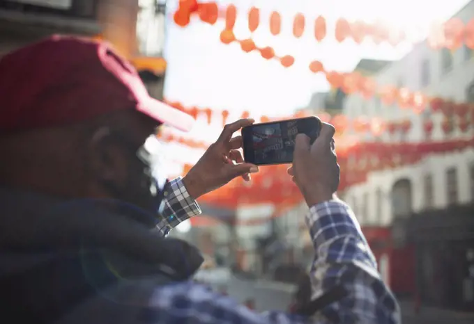 Male tourist with camera phone photographing paper lanterns in city