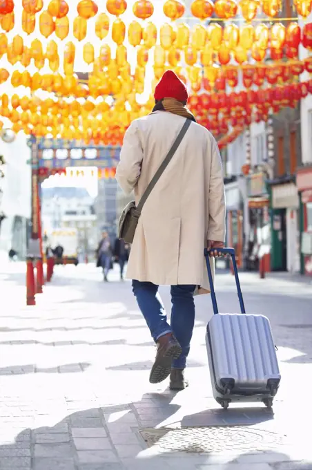 Male tourist pulling suitcase on sidewalk in Chinatown, London, UK