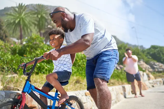 Father teaching happy son how to ride a bike on sunny boardwalk