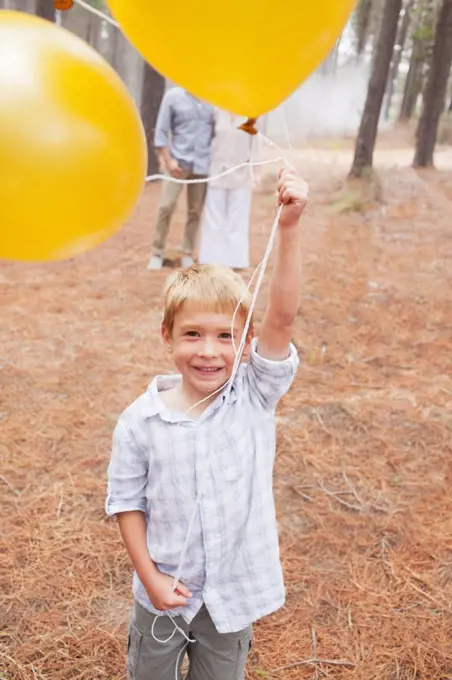 Cape Town, South Africa, Portrait of smiling boy holding balloons in woods with parents in background