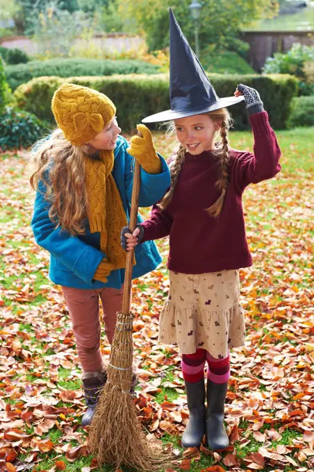 Girls playing with witch's hat and broom outdoors,belmonthouse, UK