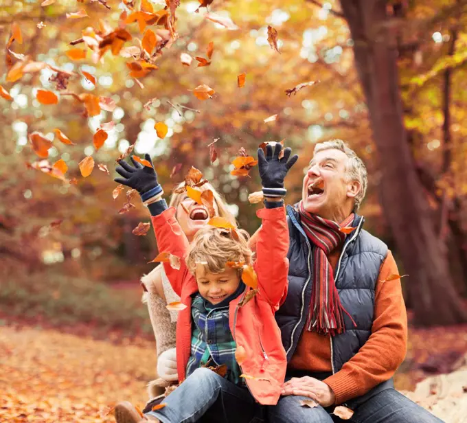 Older couple playing with grandson in autumn leaves,London, UK