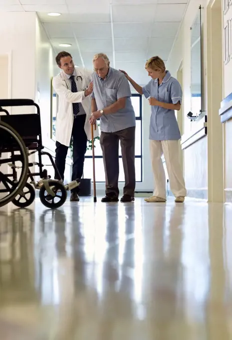 Doctor and nurse helping older patient walk in hospital